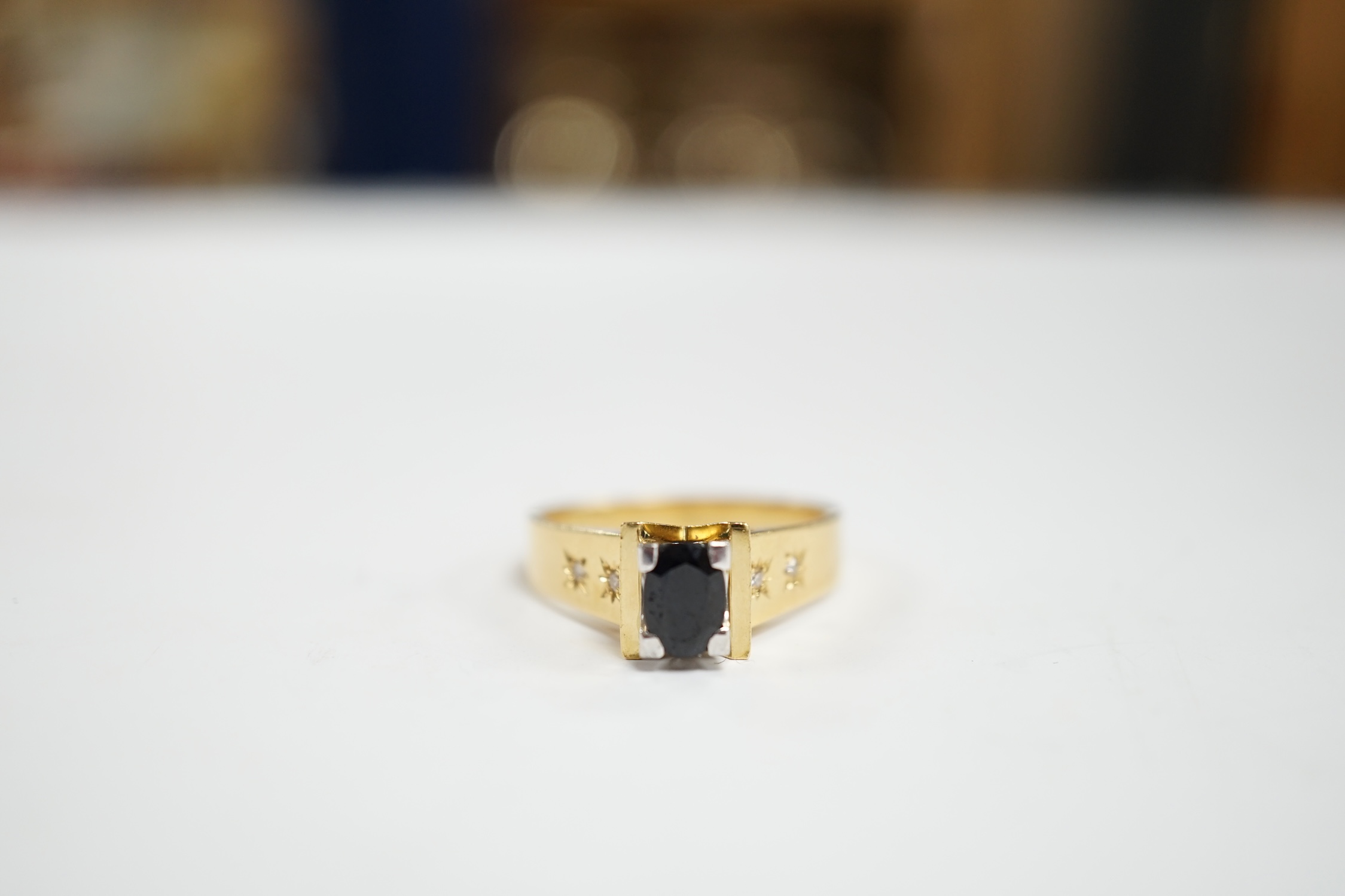 An 18ct and single stone oval cut sapphire set dress ring, with four stone gypsy set diamond chip shoulders, size R, gross weight 7.2 grams.